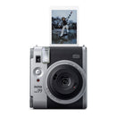 A silver and black Instax Mini 99 instant camera with a printed photo of a snowboarder emerging from the top, shown against a solid white background.