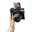 Instant camera held by a hand with a printed photo on a white background