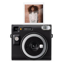 A black instax camera with silver details and a portrait photo in the eject slot on top.