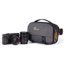LowePro Trekker Lite HP 100 compact gray camera bag with adjustable strap next to camera and lens