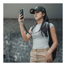 A woman holds her phone up to take a photo. The phone is attached to the PGYTECH LinkGo neck strap.