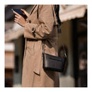 A person in a beige coat reviews their phone while wearing the PGYTECH OneGo Classic in black