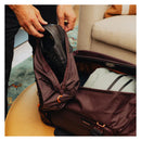 Person placing a brown leather shoe into a Peak Design Shoe Pouch inside a matching brown travel bag.