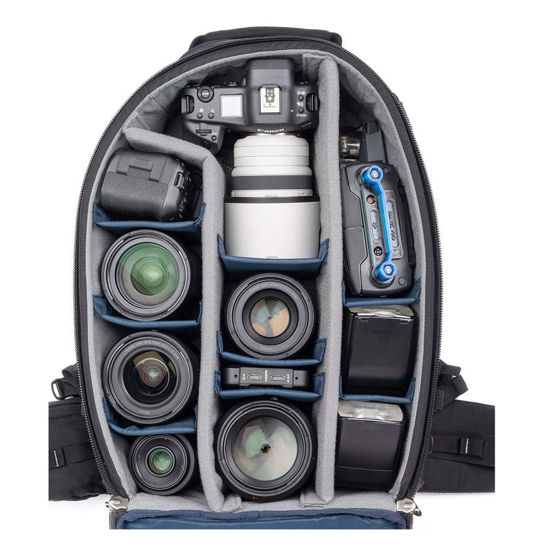 Open ThinkTank FirstLight camera backpack showing organized compartments with DSLR camera, multiple lenses, batteries, and accessories inside