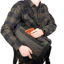 Person holding a slim black Thinktank Backlight Sprint camera backpack with orange cloth in front pocket, wearing checkered shirt
