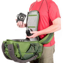 Person in red shirt demonstrating green Mindshift BackLight 18L camera backpack with rear-panel access to camera gear
